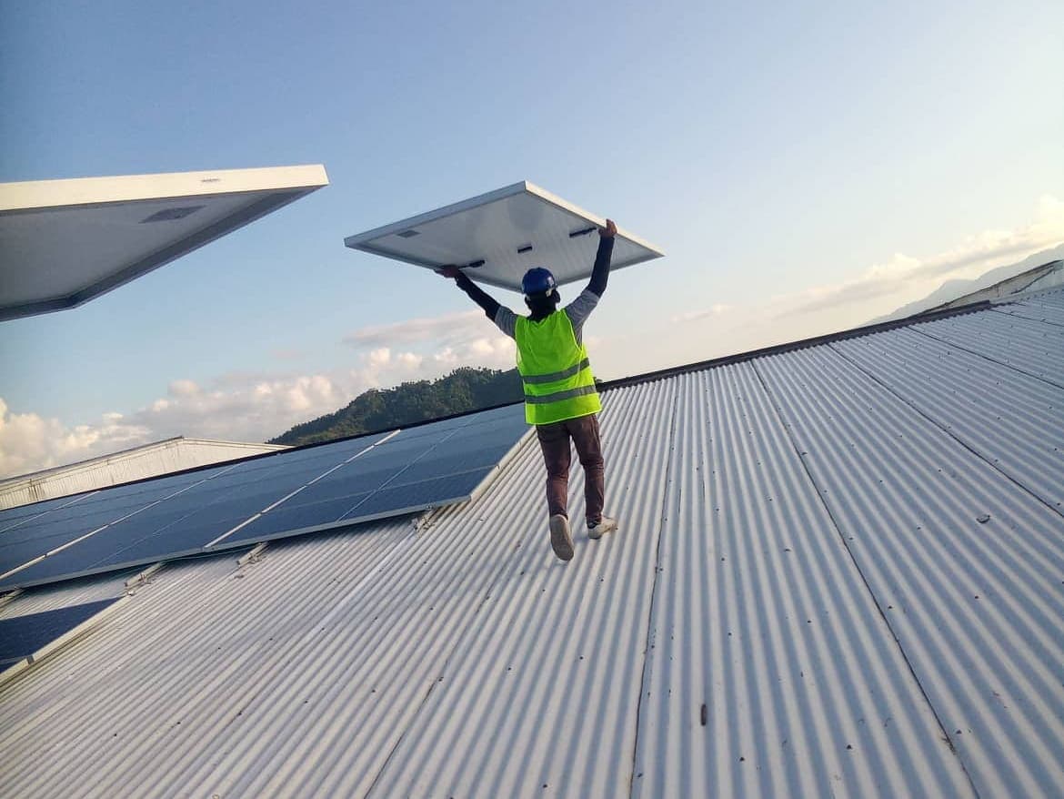 A Magnus installer carrying a photovoltaic module across a commercial roof